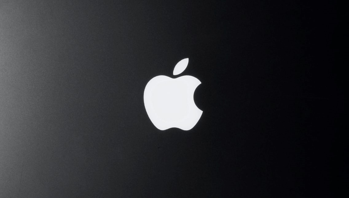 The Apple logo on a Macbook in a dark room